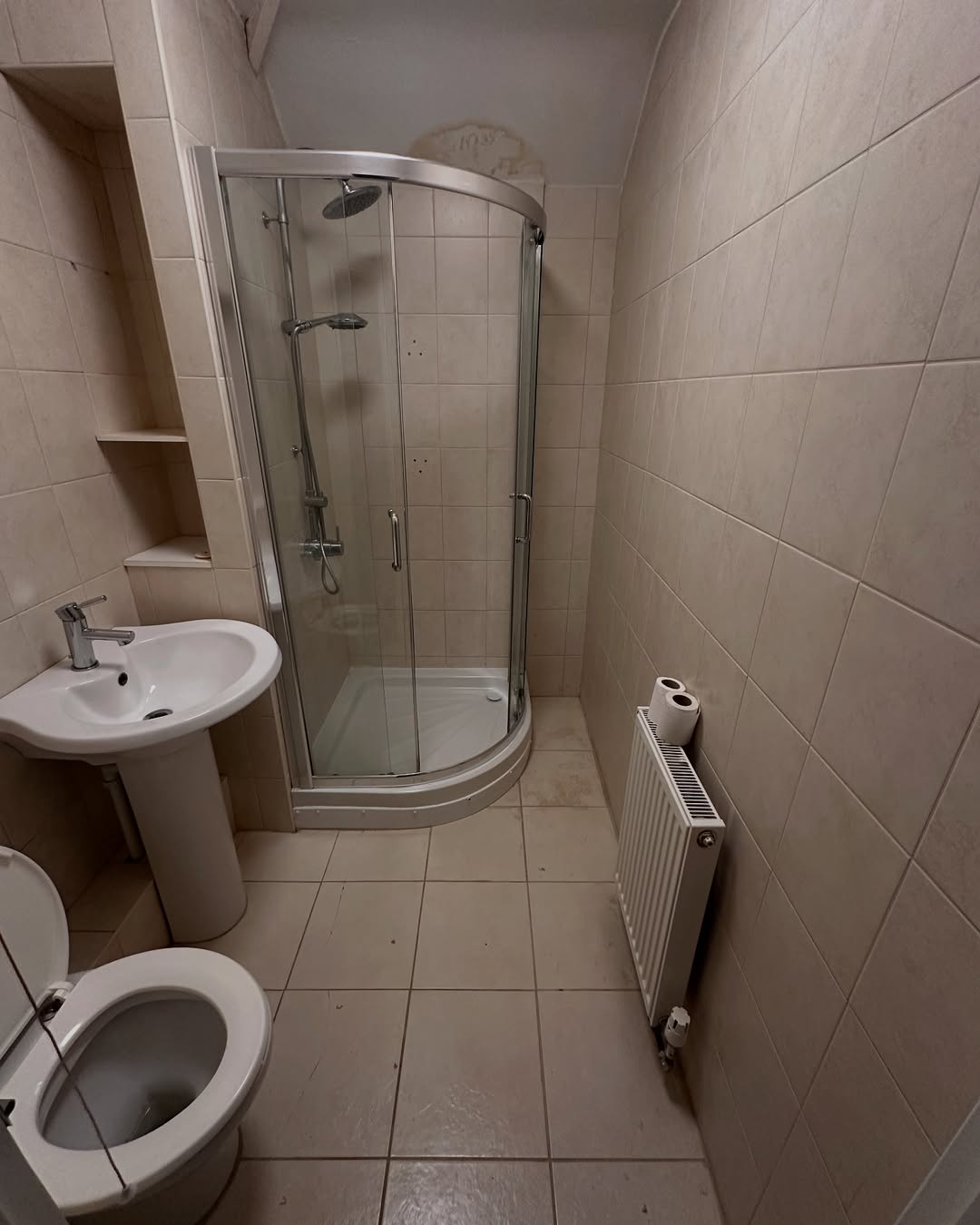 Small bathroom before renovation with older beige tile and curved shower